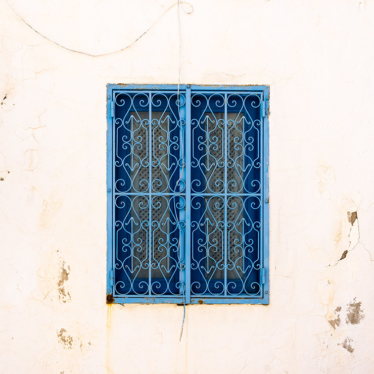 Blue window with ornate wrought iron grille set in a weathered white wall in Sidi Bou Said, Tunisia.