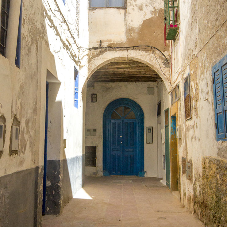 Blue arched door at the end of a sunlit alley in Essaouira’s medina.