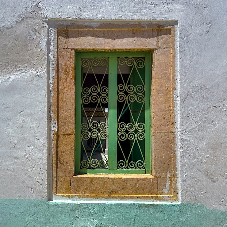 Green window with decorative iron grille set in a stone frame on a whitewashed wall in the Medina of Tunis.