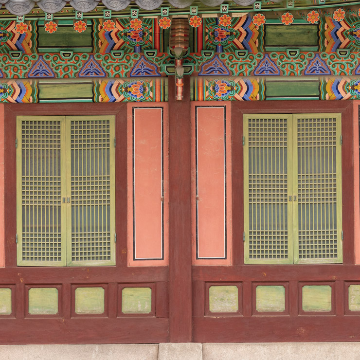 A window detail from a palace in Seoul, South Korea includes rich, colorful details and green windowshades.