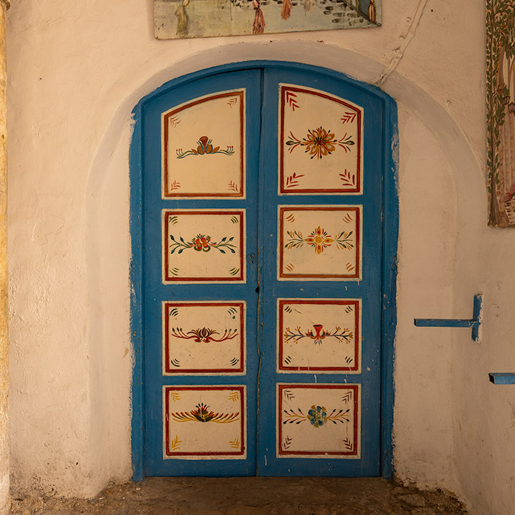 Ornate blue wooden door with hand-painted floral motifs in red, yellow, and green, located in the Medina of Tunis.