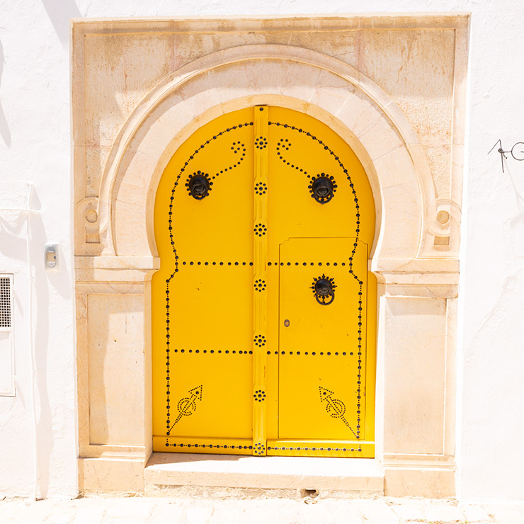 Bright yellow arched door with traditional black studded motifs set in a pale stone frame in Sidi Bou Said, Tunisia.