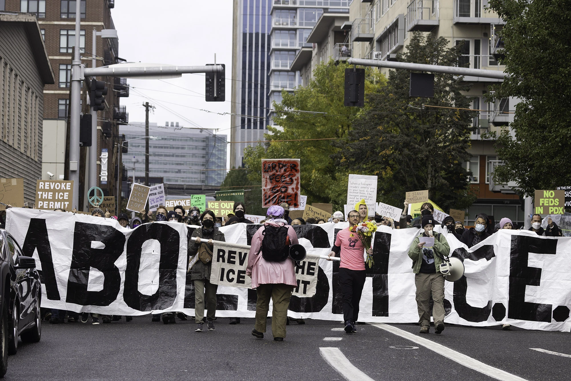 Hundreds of Portland protesters march toward the federal ICE building carrying a massive white banner reading 'ABOLISH ICE' and dozens of handmade signs demanding justice, accountability, and the revocation of ICE's permit.