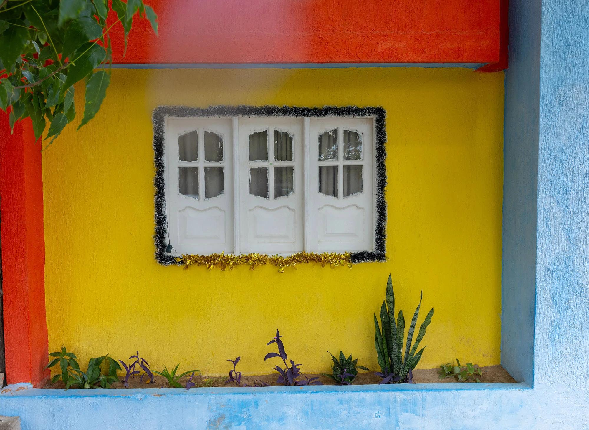 A sunlit window in the village of Camarones, Colombia is dressed with red tinsel and handmade decorations for the Christmas season. The festive colors contrast with the simple adobe wall, capturing a quiet holiday spirit on the Guajira Peninsula.