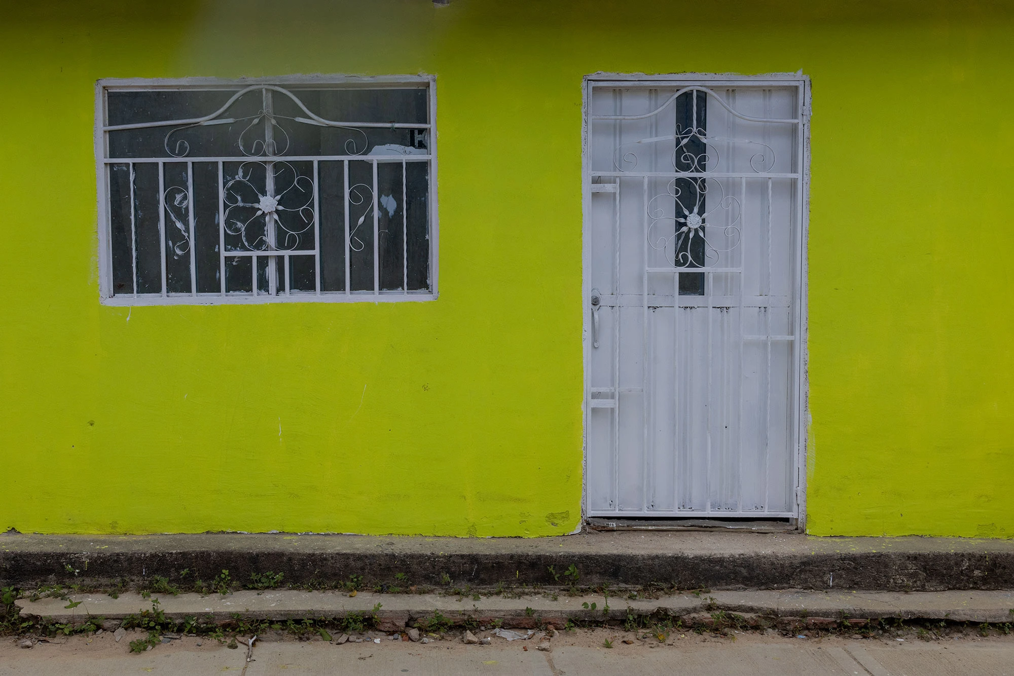A lime green door and its matching shuttered window brighten the facade of a rustic adobe home in Camarones, La Guajira. The cheerful color contrasts with the weathered wall, evoking the character of Colombia's remote desert coast.