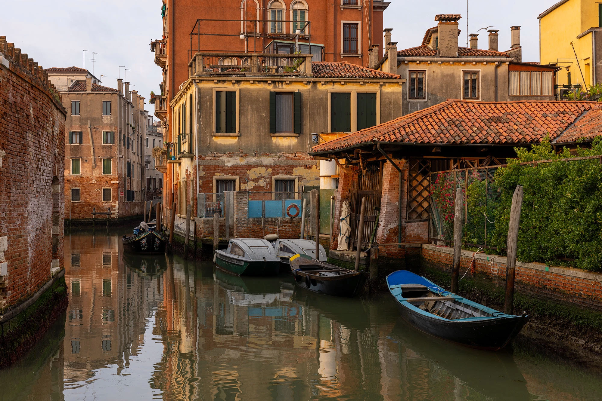 A serene, early morning view of a Venice canal in Cannaregio, with soft light illuminating the colorful buildings and calm water.